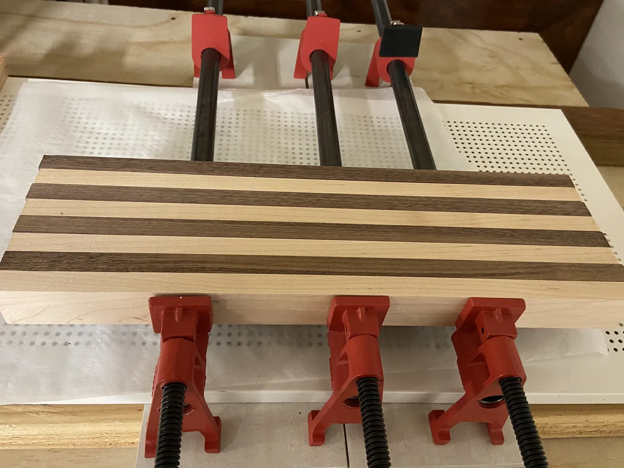 Strips of maple and walnut clamped edge to edge on a workbench, three pipe clamps above the panel and three below.